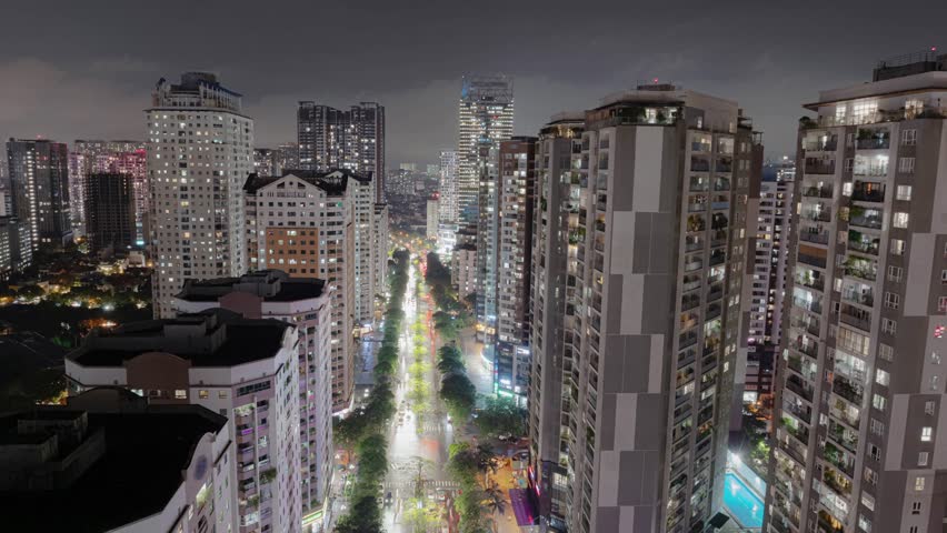Hanoi skyline framed by tall apartment towers, illuminated street stretching through city.