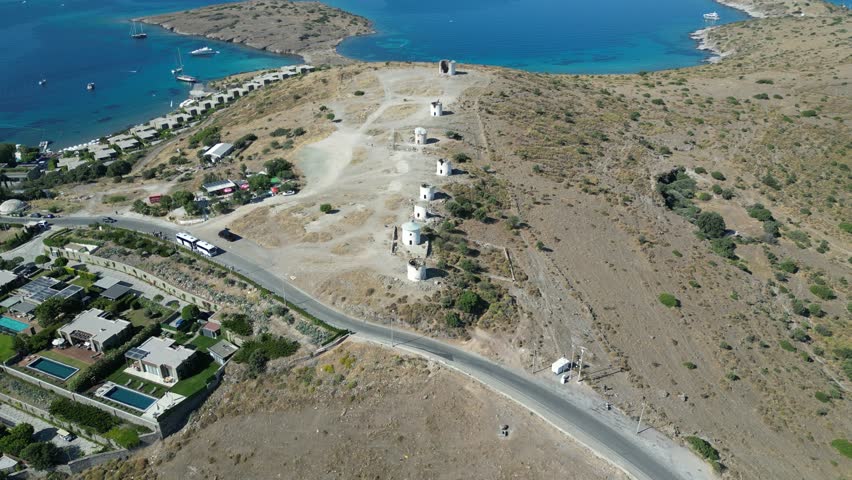 Aerial view of the iconic Bodrum windmills dotting a sun-drenched hillside overlooking the azure sea and yachts, Bodrum, Mugla, Turkey.