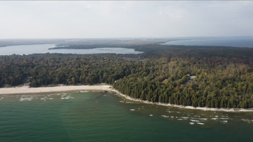 The golden sands of Whitefish Dunes curve beside emerald forest and green-blue lake waters, revealing the natural beauty of Door County’s eastern shoreline from above.