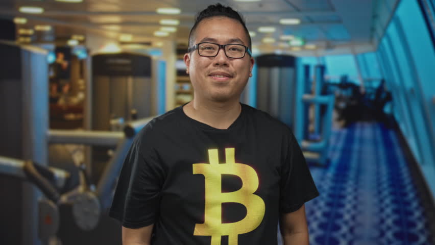 Man wearing bitcoin t shirt extends hand for handshake in gymnasium sports center indoor workout area; cryptocurrency trust welcoming community.