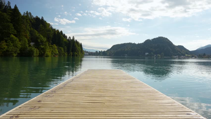 Man runs down a wooden pier and leaps into Lake Bled, capturing carefree summer vibes, static wide shot.