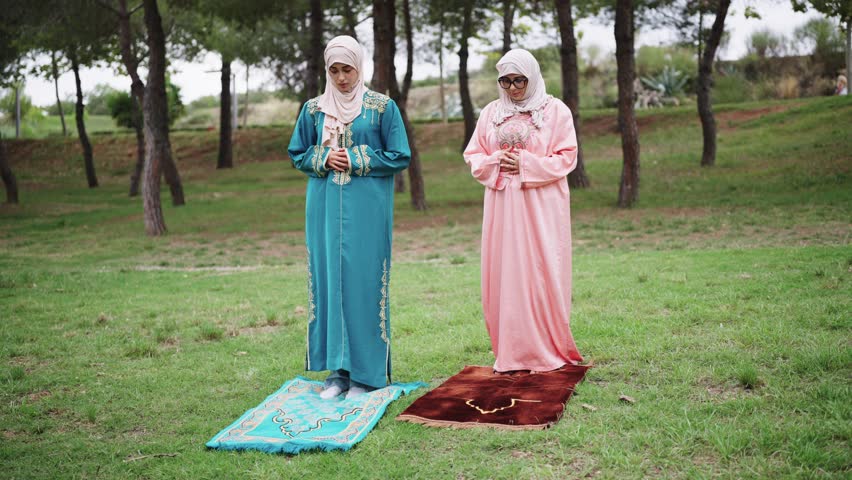 Muslim women in hijabs praying outdoors on mats