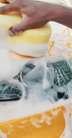 A close-up shot of a hand washing a car with a sponge and soapy water, creating a foamy effect.