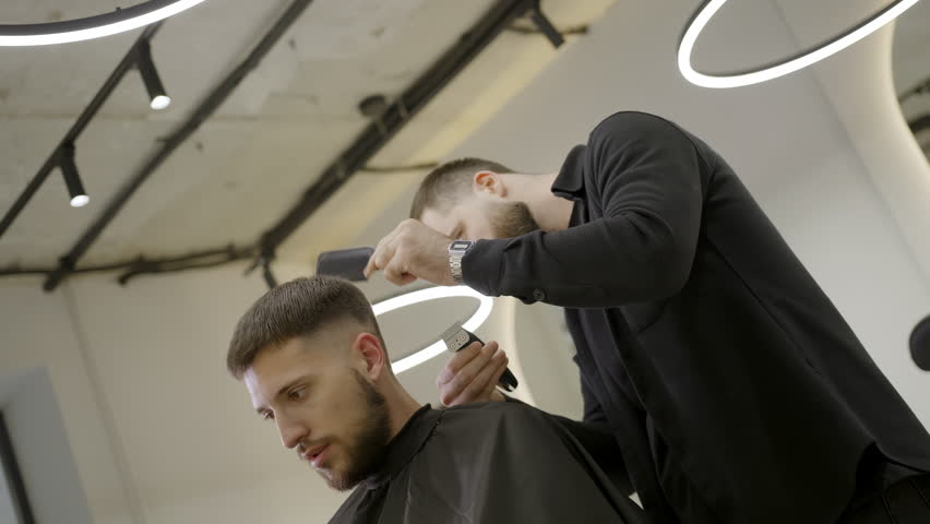 Professional barber giving haircut to male client. Clip
