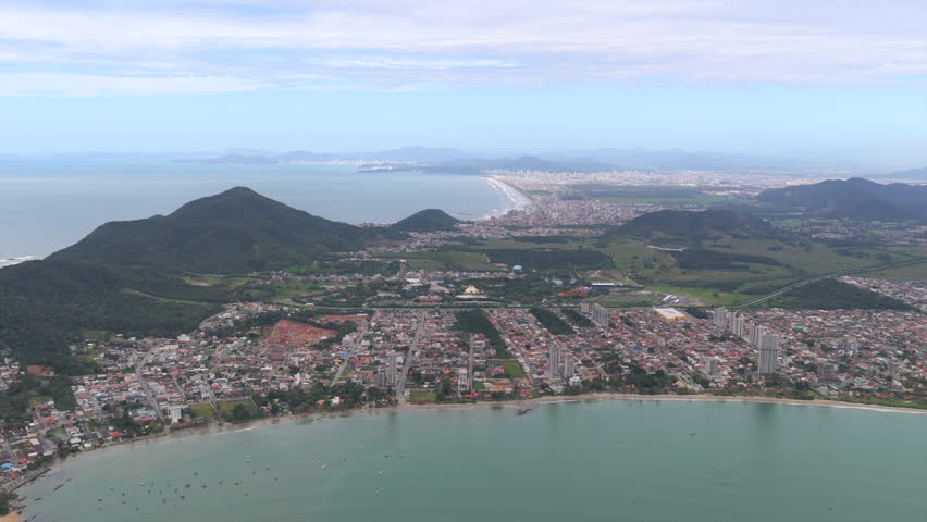 Tropical coastal Penha city with surrounding hills and distant Parque da Meia Praia shoreline from above, Santa Catarina, Brazil.