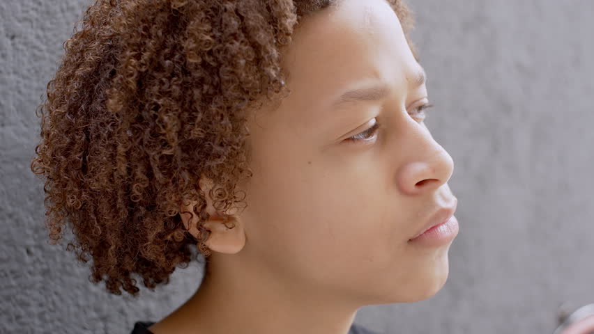 Close-Up Of Young Boy With Curly Hair Looking Up With Thoughtful Expression, Standing Near Textured Gray Wall In Quiet Moment