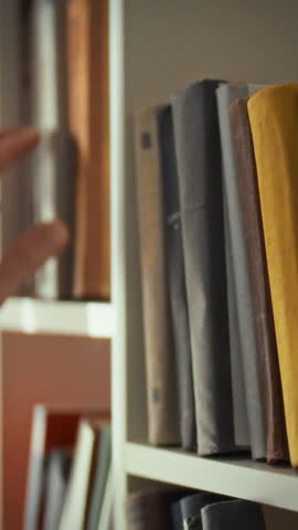 A person reaches for a book from a well-organized shelf in a warm library. This scene captures the quiet joy of selecting a new read in a peaceful environment