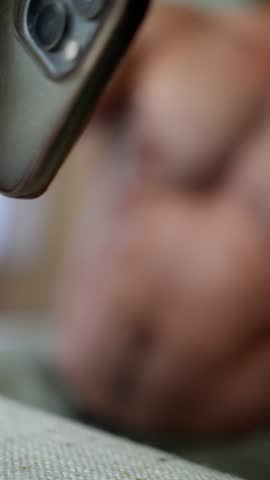 A closeup video of a muscular male torso, showcasing its athletic build in soft, warm lighting. A man with a phone in his hands writes a message in a chat. 