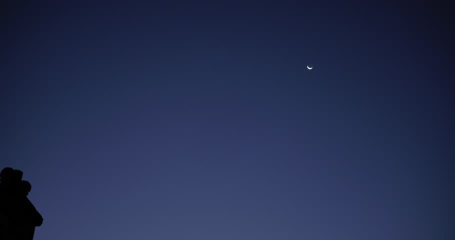Vertical panning shot of the moon over a city at dawn. From the terrace of a building.  