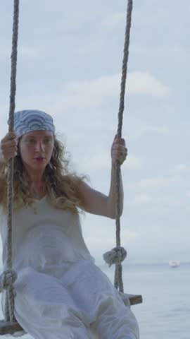 A joyful girl swings at a beach sunset, embodying freedom and carefree spirit with a smile