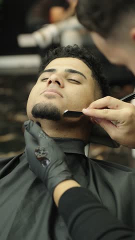 Professional barber shaving man's beard with straight razor in a barbershop