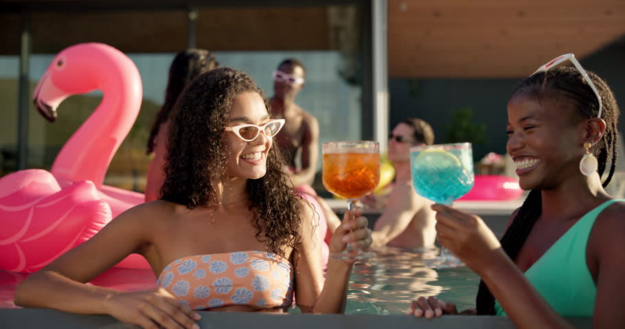 Women, friends and laughing with cheers at pool party for new year, celebration or summer vacation. Female people, drinks or cocktail with smile for break, relaxation or good vibes at luxury resort