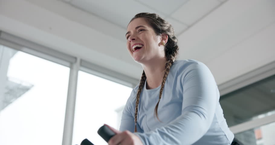 Below, woman and stationary bike for fitness at gym for exercise, cardio training and lose weight. Smile, female person and cycling on machine, endurance workout and intense performance for wellness