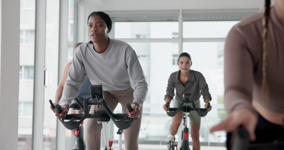 Fitness, people and stationary bike in gym for cardio exercise, endurance challenge or training. Group workout, indoor cycling and spin class with athletes in health club for performance or sports