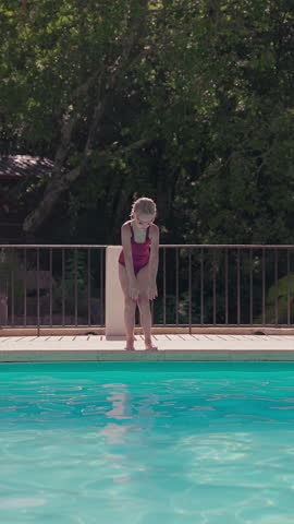 Young girl in swimsuit and goggles jumps into backyard pool on a sunny summer day creating big splash