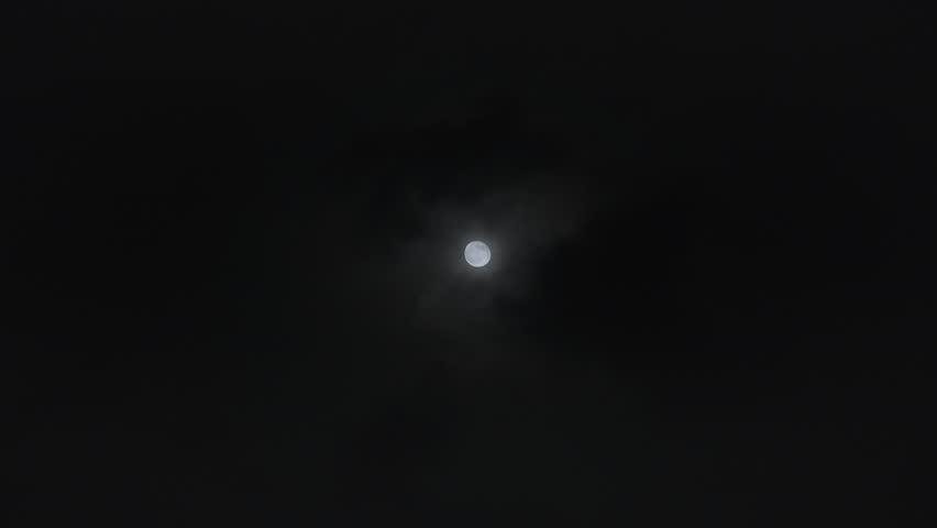 A time lapse shot of the dark monsoon or rain clouds passing in front of the moon in the night