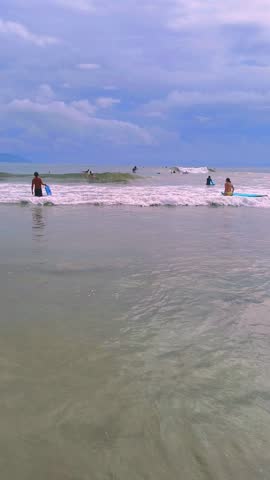 People Surfing and Wading in the Ocean on a Cloudy Day