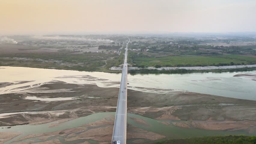 Stunning aerial drone shot of a long concrete bridge spanning a wide, shallow river with visible sandbanks at sunset or sunrise