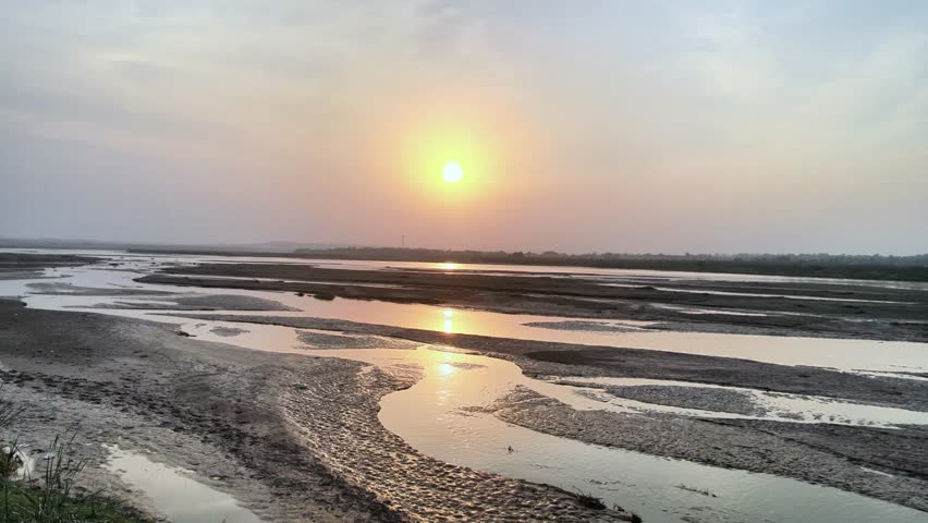 Peaceful aerial view of a river with multiple channels and sandbanks at sunset. Warm golden light reflects on water, creating a tranquil, cinematic atmosphere in a vast natural floodplain.