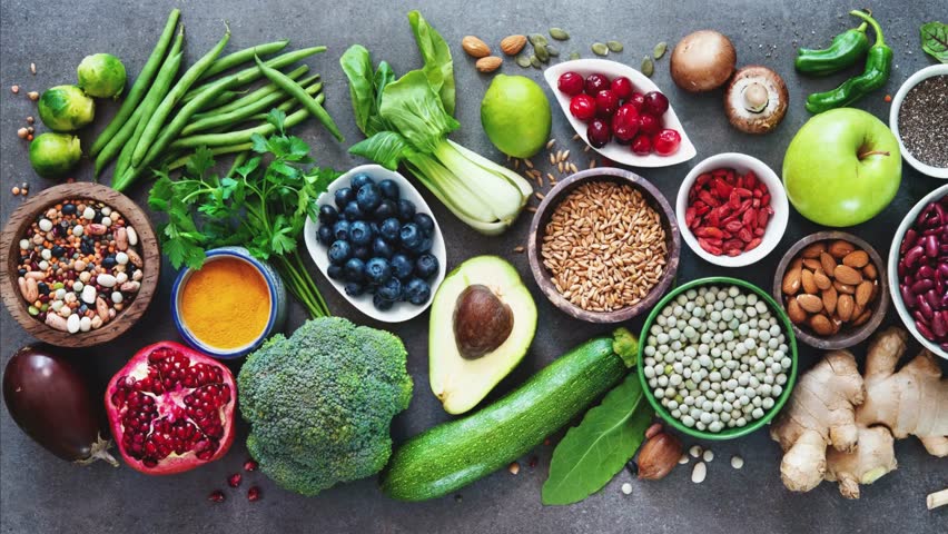 An overhead shot of a vibrant assortment of fresh fruits, vegetables, nuts, grains, and spices, promoting healthy eating and a balanced, plant-based diet on a dark background.
