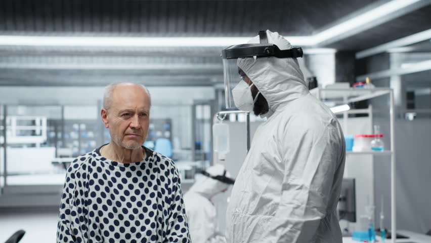 Male medic scientist treating patient with severe infection symptoms, using immunology testing in a containment lab to support vaccine development and epidemic control. Camera B.