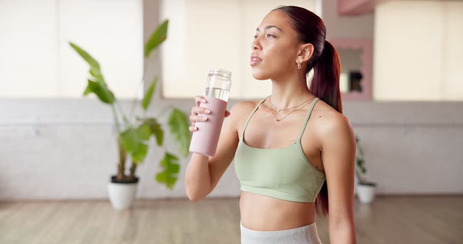 Fitness break, girl and drinking water in studio for hydration, pilates recovery and nutrition. Wellness, person or liquid bottle in health club for workout refresh, thirsty or rest from yoga routine