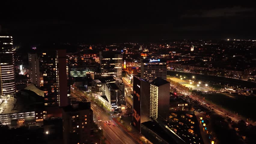 Aerial night view of Vilnius business district, featuring illuminated skyscrapers, modern glass buildings, and vibrant city lights along Konstitucijos Avenue.