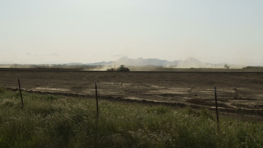 Wide show of tractor plowing dusty field 
