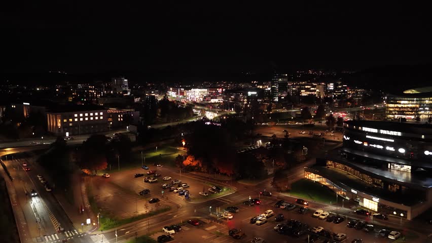 Aerial night view of Vilnius business district, featuring illuminated skyscrapers, modern glass buildings, and vibrant city lights along Konstitucijos Avenue.