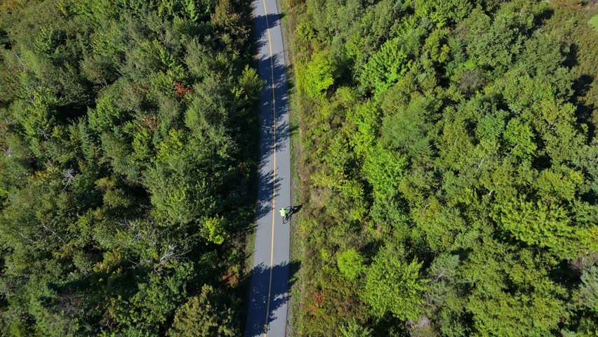 Sporty Man Rides Bicycle With Helmet Through Curved Path Between Trees And Still Lake. Stunning Summer Drone Shot For Sport, Travel, Motivation, And Outdoor Health Concepts In Nova Scotia.
