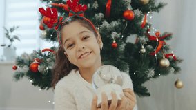 Young girl enjoys a festive moment holding a snow globe near a beautifully decorated Christmas tree in a cozy living room - Powered by Shutterstock - Get 15% off with code: PIKWIZARD15
