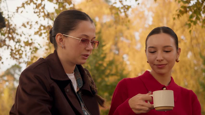 Warm fall portrait style frame, women sitting on blanket sip hot coffee or tea, soft light, golden foliage and minimal composition.
