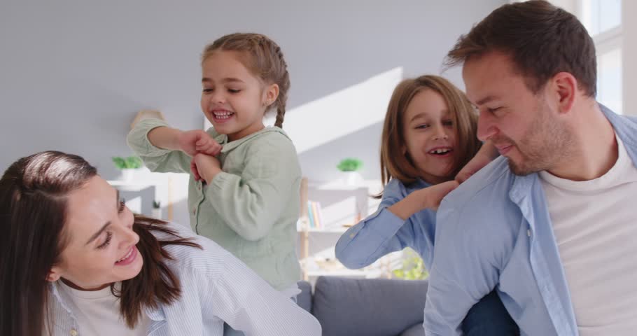 Happy young cheerful family having fun with children riding them on back in living room at home. Mother and father spending time together with kids. Family time concept. 4k video. Slow motion video.