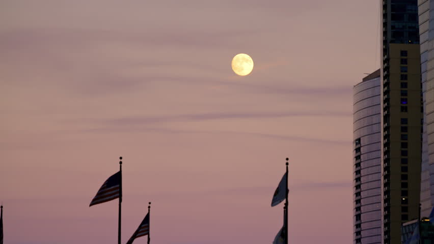 Silhouettes of flags fluttering in the wind on the bridge and high-rise buildings at the evening time, with moon on purple sky background. Chicago city life atmosphere.
