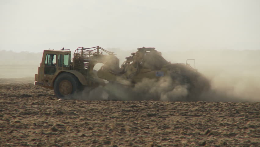Earth mover drives through dusty field