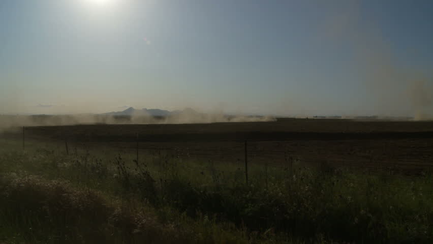 Wide shot of farmland being plowed by tractors stirring up dust