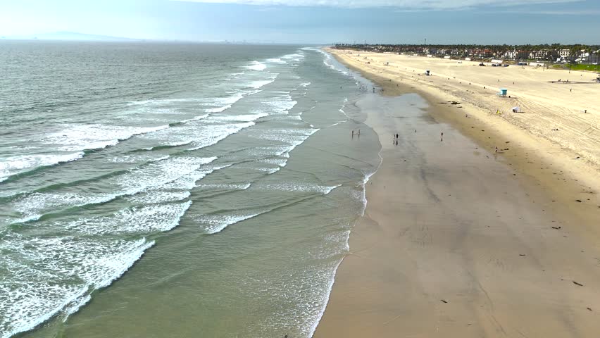 Drone footage of Huntington Beach, California showing ocean waves, coastline, and beachfront buildings on a sunny day.