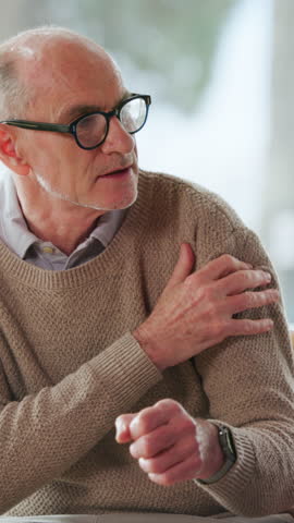 Senior man, talking and arm pain at house with discomfort, muscle strain and arthritis symptoms. Elderly person, explaining and massage shoulder of joint stiffness, sore inflammation and fibromyalgia