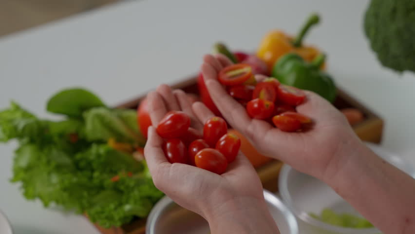 Hands holding cherry tomatoes with nutrient callouts like lycopene, vitamin A, and beta carotene, surrounded by fresh greens in a kitchen setting.