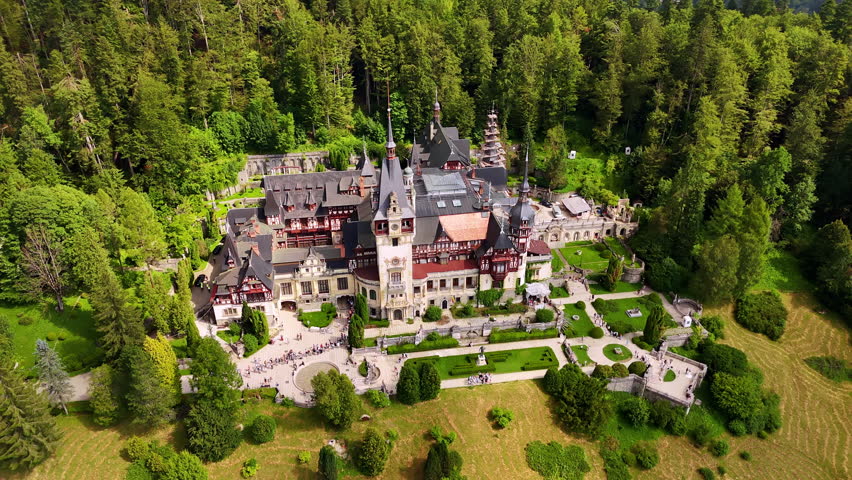 Beautiful scenery of the Peles Castle in Prahova County, Romania. Lush green pine tree wood grows around. Aerial view.