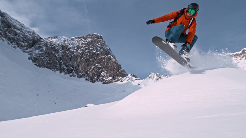 Off Piste Snowboarder Jumping. Super Slow Motion, 1000 fps. Snowboarding on Free Ride off Piste Slope on Sunny Day With Clear Blue Sky in European Alps Mountains, Austria.