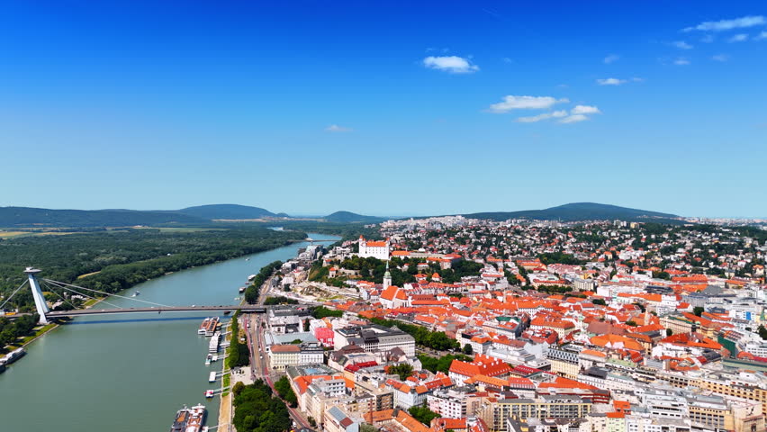 Rising above the Danube and old town of Bratislava, Slovakia. View on the UFO Bridge over the river. Vast scenery of the city from drone.