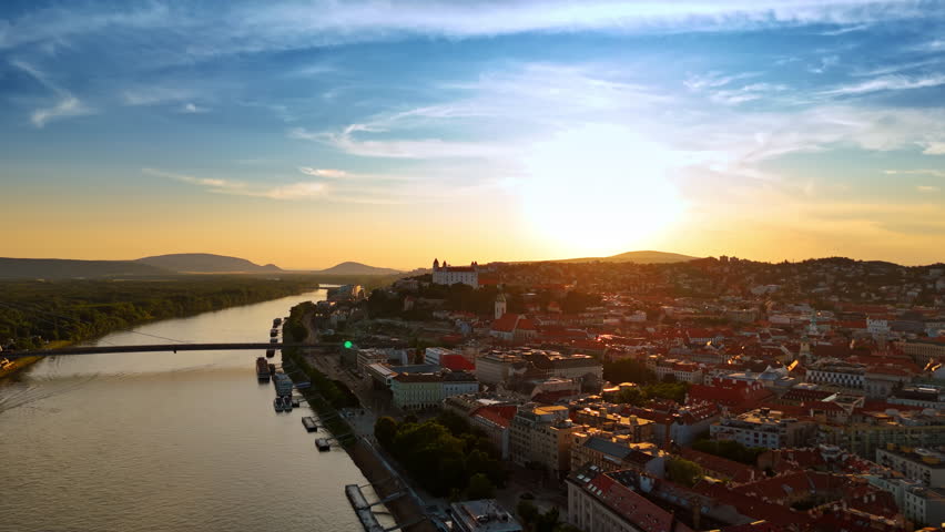 Setting sun lights the cityscape of old town of Bratislava, Slovakia. Drone footage over the Danube waterscape and city scenery at sunset.