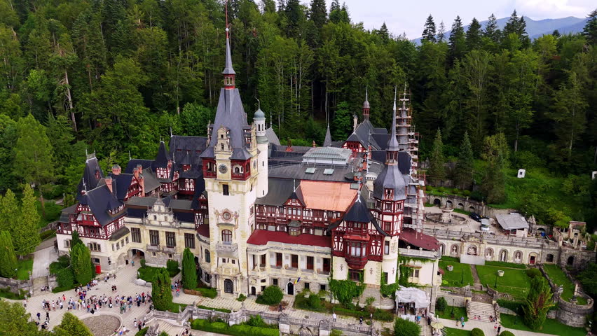 Multiple people stand in a line at the entrance to the Peles Castle in Prahova County, Romania. Aerial view on the stunning architecture at the backdrop of green forest.