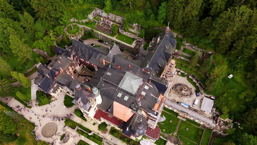Flight over the roofs of the Peles Castle in Prahova County, Romania. Multiple people visit the landmark and walk by the territory.
