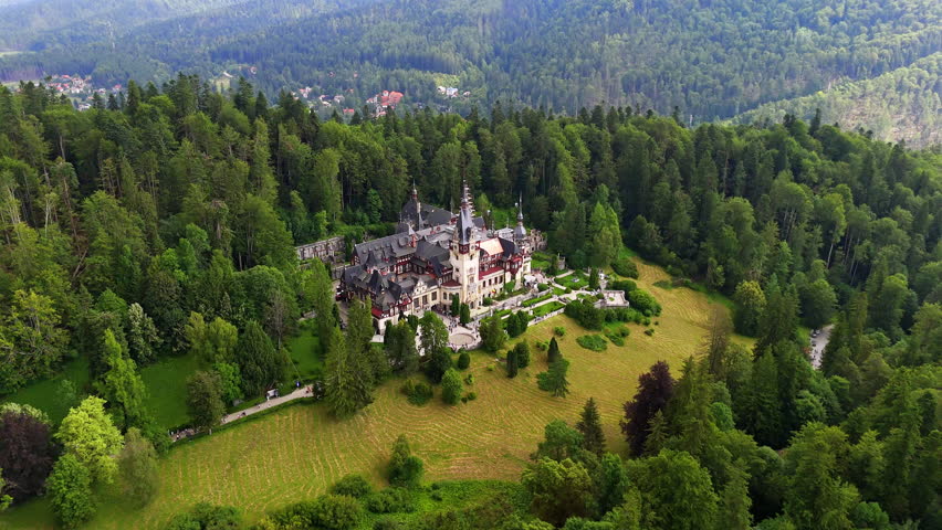 Gorgeous castle on the top of the mountain surrounded by the lush green pine tree wood. Aerial view on the Peles Castle in Prahova County, Romania.