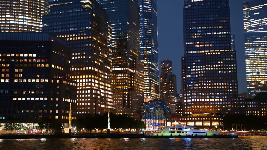 River cruise along the luminous waterfront of New York, USA. Low angle view at the high-rise buildings with switched on lights.