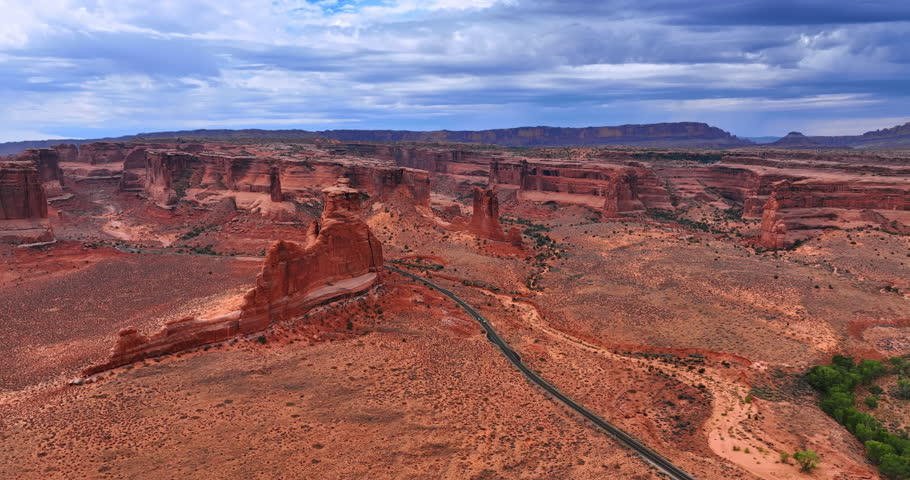 Flying closer to the highway crossing the arid desert. Approaching the steep canyons with no vegetation in the Arches National Park, Utah, USA.