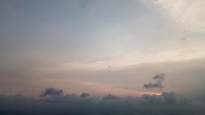 Beautiful sunset over the ocean with dramatic dark clouds and soft orange light, creating a peaceful yet moody natural landscape background