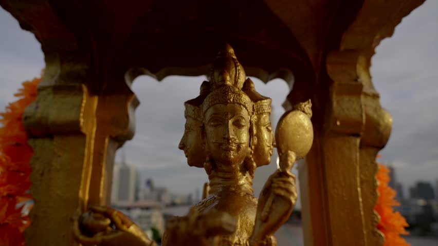Golden statue of Phra Phrom, the Thai representation of Brahma, the creator of Hinduism, located on the roof of a skyscraper overlooking the city of Bangkok.